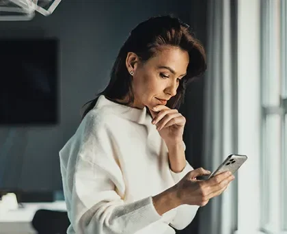 MED - Mecanismo Especial de Devolução - Foto de uma mulher em casa olhando para a tela do celular com a expressão preocupada e concentrada